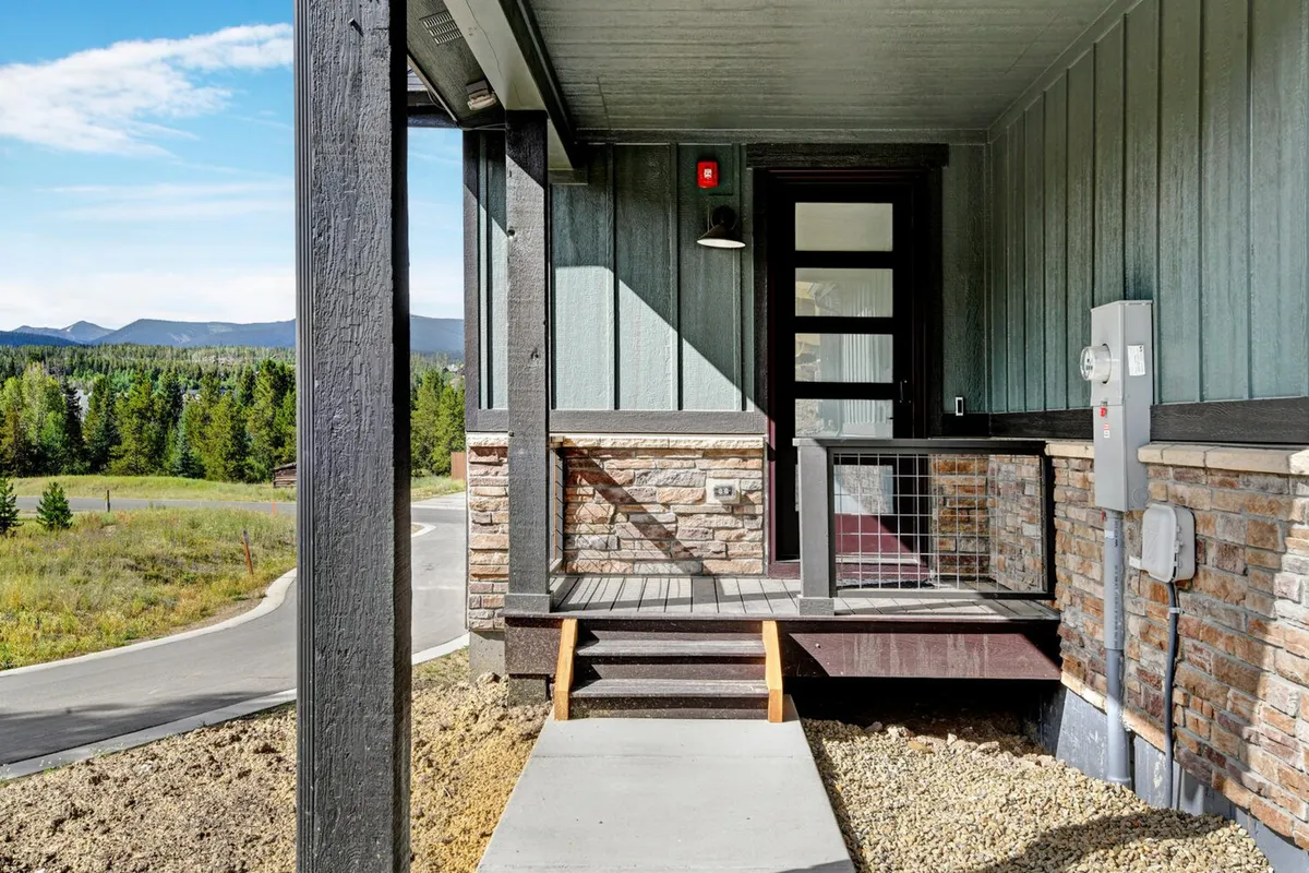 The image presents a welcoming entrance with a front door framed by stone accents and landscaped views stretching into the distance. The inviting porch suggests relaxation and a sense of arrival, hinting at the comfort and privacy awaiting inside.
