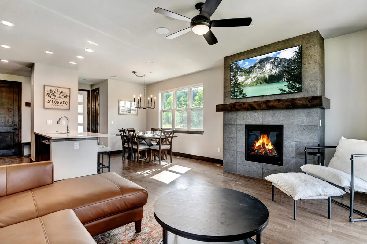A cozy dining table set near a fireplace and large windows, with views outside and a TV featuring mountain scenery. The space is ideal for hosting dinner parties, family meals, and relaxing evenings.