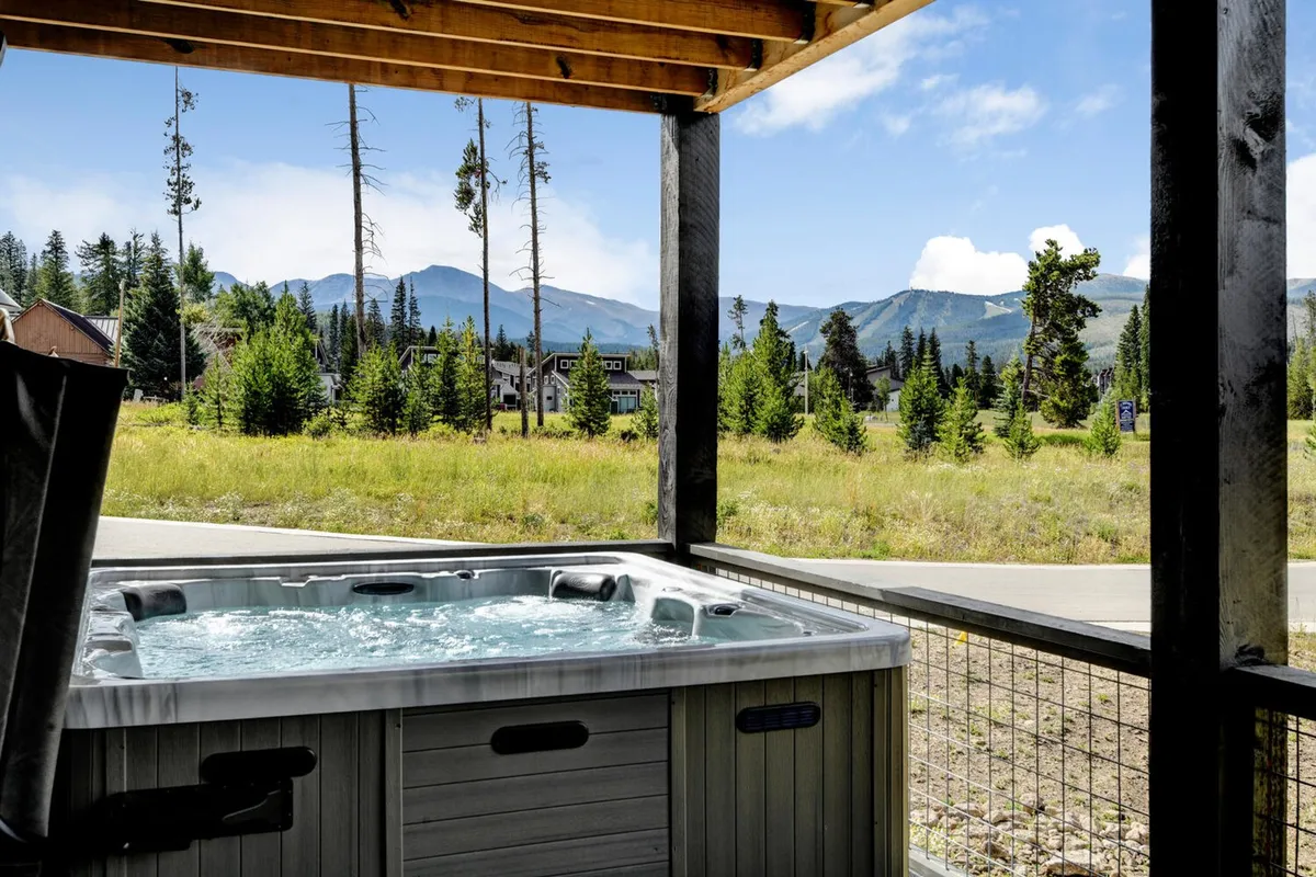 An outdoor hot tub set against a backdrop of mountain views and tall trees, offering a tranquil space for relaxation. The area is perfect for soaking under the stars after a long day of adventure, with nature as the perfect peaceful companion.