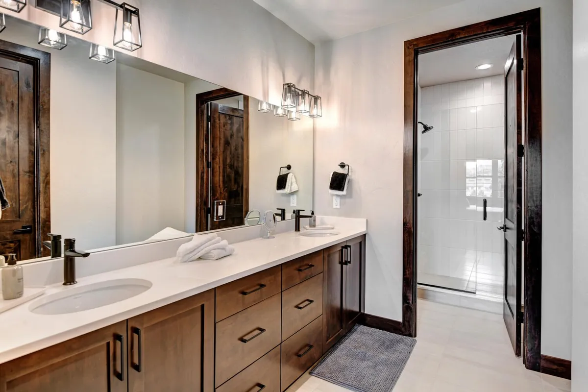A spa-inspired bathroom showcasing a double sink vanity with wooden cabinetry, large mirrors, and a glass-walled shower stall. The space feels bright and tranquil, with elegant fixtures and plenty of room for morning or evening routines.