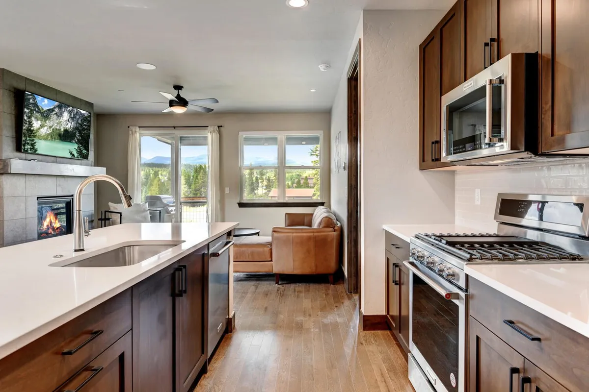 A view of the kitchen island with stainless steel appliances, a fireplace, large windows, and a comfortable seating area, blending culinary and social spaces for a seamless hosting experience.