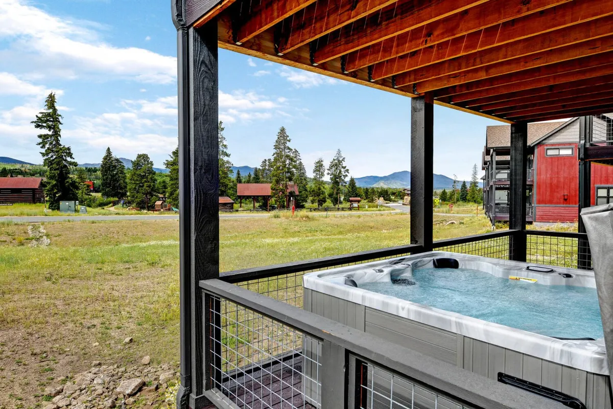 A private outdoor hot tub on a deck overlooking a sweeping mountain vista. The inviting bubbling water beckons after a day in the snow, with tranquil natural surroundings enhancing the sense of relaxation and exclusivity.