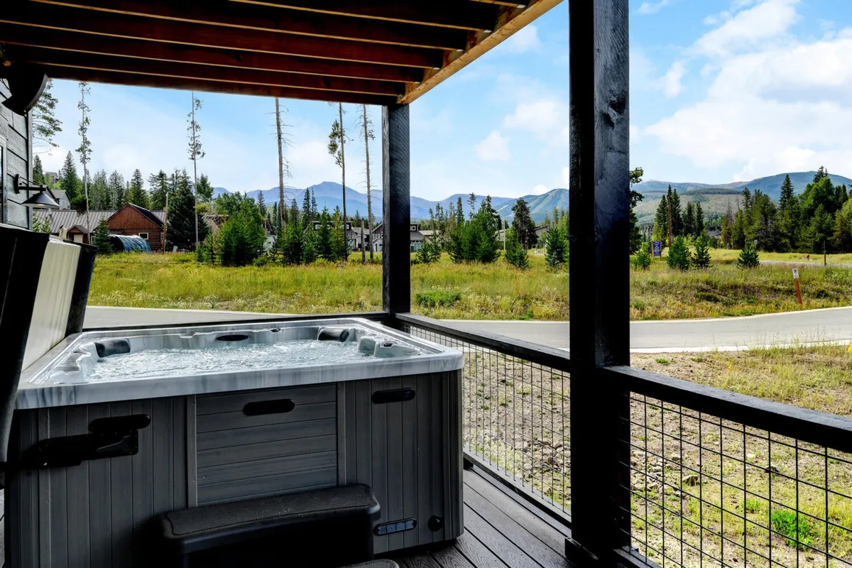 This image showcases a luxurious private hot tub set on a deck overlooking a breathtaking mountain view, surrounded by lush greenery. The tranquil atmosphere highlights the experience of relaxing in a high-end amenity with nature all around, emphasizing exclusivity and comfort.