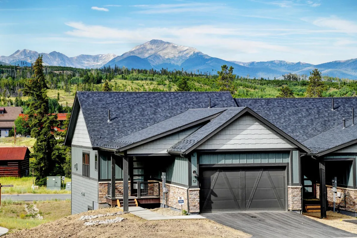 The image showcases a striking modern mountain chalet set against the breathtaking backdrop of the Colorado Rockies. The home's clean architectural lines and large windows are complemented by lush landscaping, inviting outdoor living spaces, and expansive views. The scene evokes a sense of tranquility and connection with nature, perfect for relaxation or gathering with family and friends.