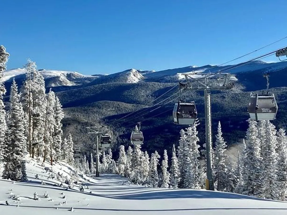 This image captures ski lift gondolas gliding above snow-covered slopes, with distant mountains and pine trees completing the breathtaking alpine scene. The snow-covered terrain and lifts are busy with skiers and snowboarders, conveying the excitement of winter sports in a pristine mountain setting.